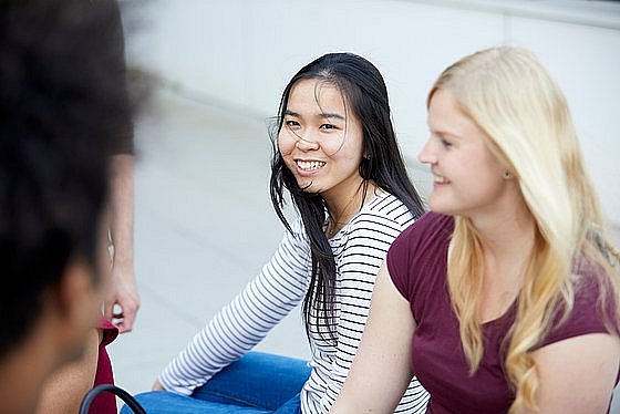 Zwei weibliche Studierende sitzen nebeneinander und lachen