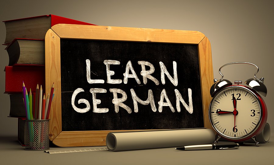 Eine Kreidetafel mit der Aufschrift "Learn German" auf einem Schreibtisch.